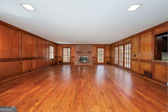 unfurnished living room featuring a brick fireplace, wood walls, plenty of natural light, and hardwood / wood-style flooring