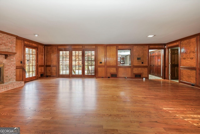 unfurnished living room with hardwood / wood-style flooring, a brick fireplace, and wood walls