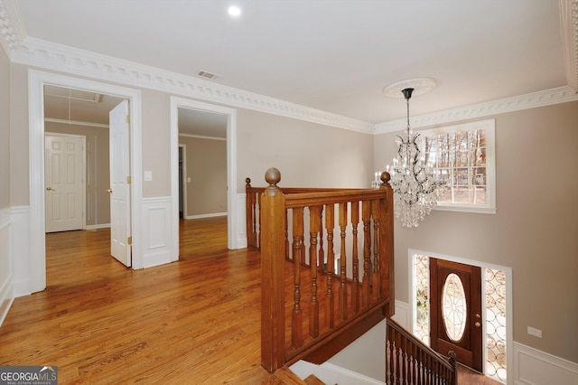 staircase featuring wood-type flooring, crown molding, and a chandelier