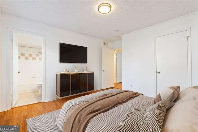 bedroom with ornamental molding, light wood-type flooring, a textured ceiling, and ensuite bath