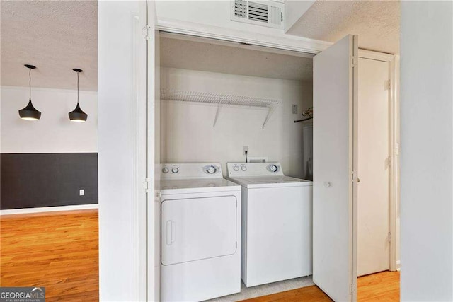 laundry room featuring washer and clothes dryer, light hardwood / wood-style flooring, and a textured ceiling