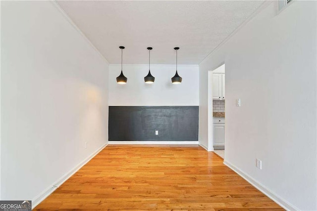 unfurnished dining area with light wood-type flooring, ornamental molding, and a textured ceiling