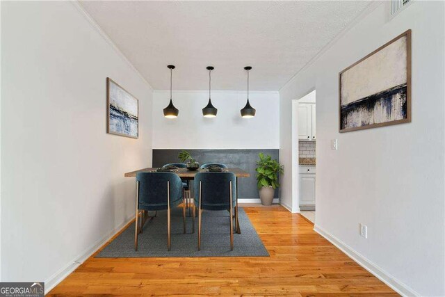 dining space with ornamental molding and light hardwood / wood-style flooring