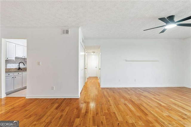 empty room with ceiling fan, sink, a textured ceiling, and light wood-type flooring