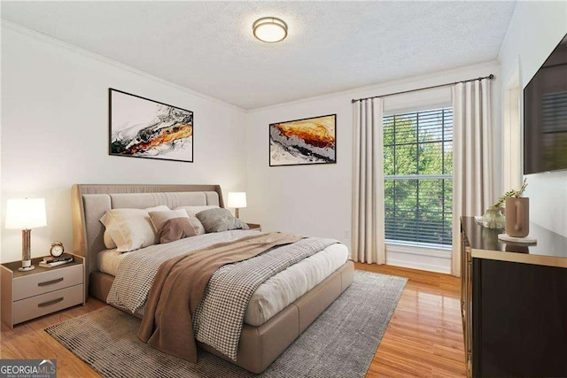 bedroom featuring light hardwood / wood-style floors, crown molding, and a textured ceiling