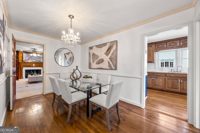 dining space featuring ceiling fan with notable chandelier, ornamental molding, sink, and light wood-type flooring