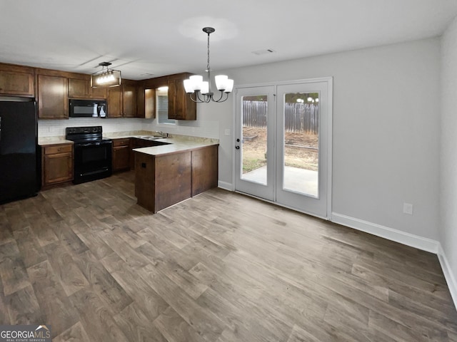 kitchen with an inviting chandelier, kitchen peninsula, hardwood / wood-style floors, decorative light fixtures, and black appliances