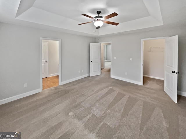 unfurnished bedroom with a raised ceiling, ceiling fan, light colored carpet, and a spacious closet