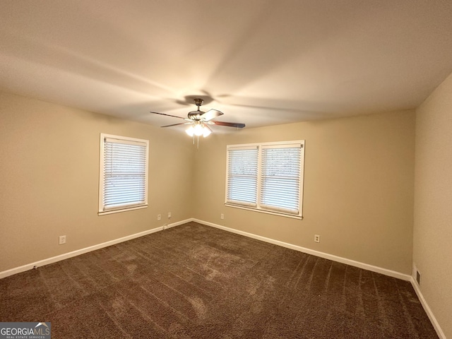 empty room featuring ceiling fan, a healthy amount of sunlight, and dark carpet