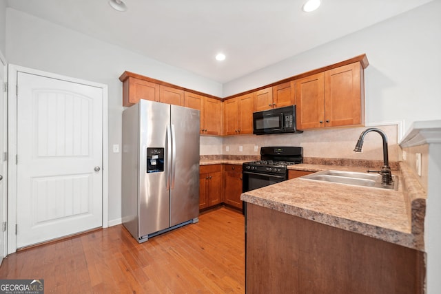 kitchen with kitchen peninsula, sink, light hardwood / wood-style flooring, and black appliances