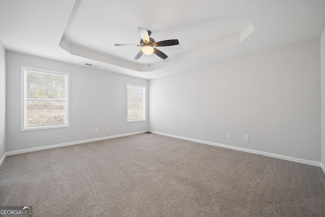 carpeted spare room with a tray ceiling and ceiling fan