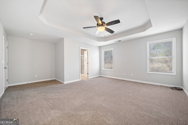 unfurnished bedroom featuring a tray ceiling, multiple windows, ceiling fan, and light colored carpet