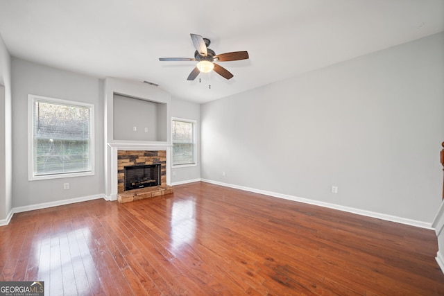 unfurnished living room with ceiling fan, a stone fireplace, and wood-type flooring