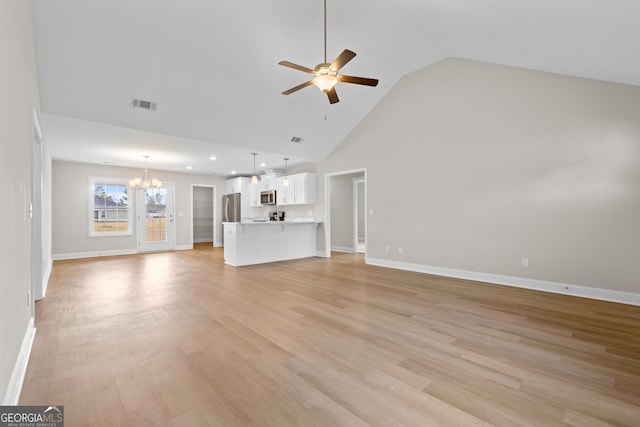 unfurnished living room with ceiling fan with notable chandelier, light hardwood / wood-style floors, and high vaulted ceiling