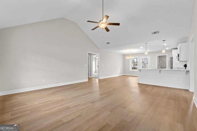 unfurnished living room featuring ceiling fan with notable chandelier, light wood-type flooring, and high vaulted ceiling