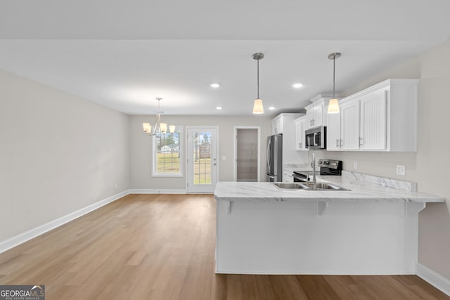 kitchen with pendant lighting, white cabinets, stainless steel appliances, and light hardwood / wood-style floors