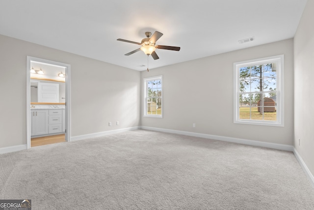 unfurnished bedroom with ceiling fan, light colored carpet, and ensuite bath