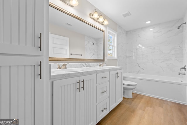 full bathroom featuring hardwood / wood-style floors, vanity, tiled shower / bath combo, and toilet