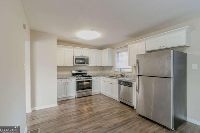 kitchen with light stone countertops, white cabinetry, sink, stainless steel appliances, and dark hardwood / wood-style flooring