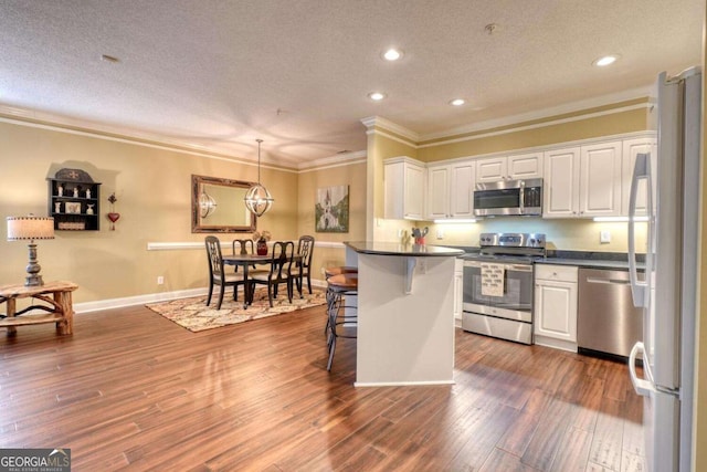 kitchen with dark hardwood / wood-style floors, pendant lighting, a breakfast bar, white cabinets, and appliances with stainless steel finishes