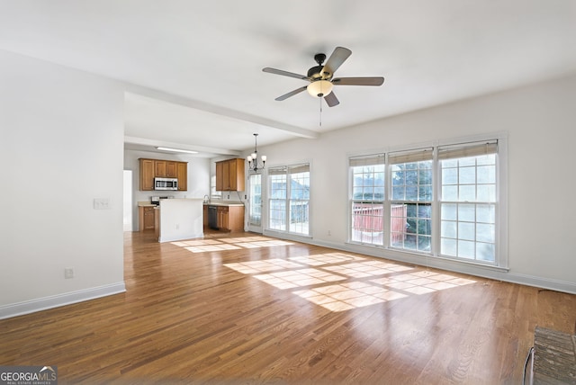 unfurnished living room featuring ceiling fan with notable chandelier, light hardwood / wood-style flooring, and plenty of natural light