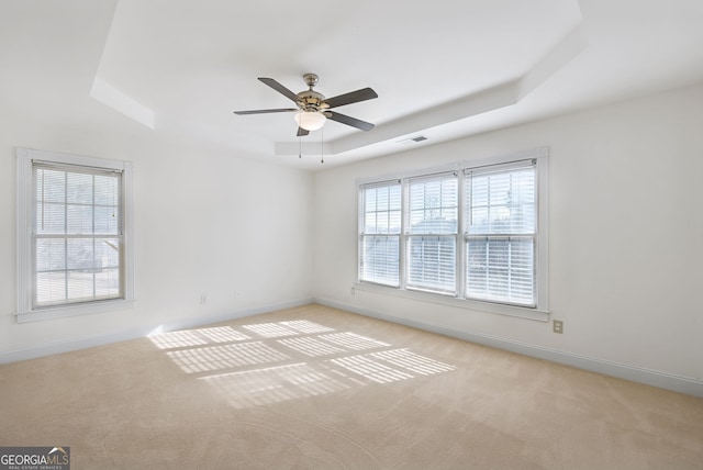 unfurnished room with ceiling fan, a tray ceiling, and a healthy amount of sunlight