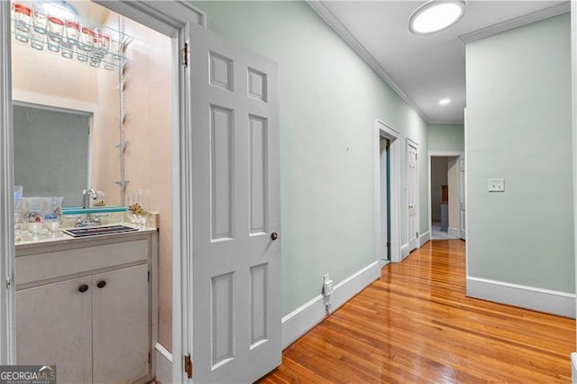 hallway featuring sink, crown molding, and light hardwood / wood-style flooring