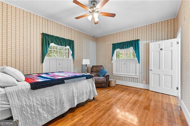 bedroom with hardwood / wood-style floors, ceiling fan, ornamental molding, and multiple windows