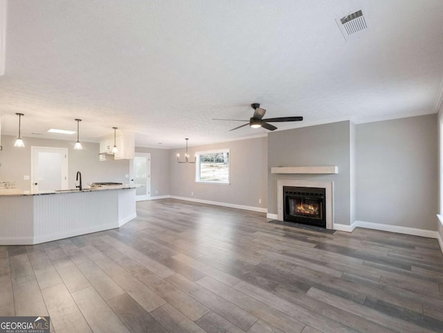 unfurnished living room featuring sink, crown molding, ceiling fan, a textured ceiling, and dark hardwood / wood-style flooring