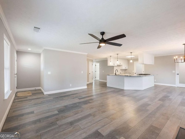 unfurnished living room featuring ornamental molding, ceiling fan with notable chandelier, a textured ceiling, and dark wood-type flooring