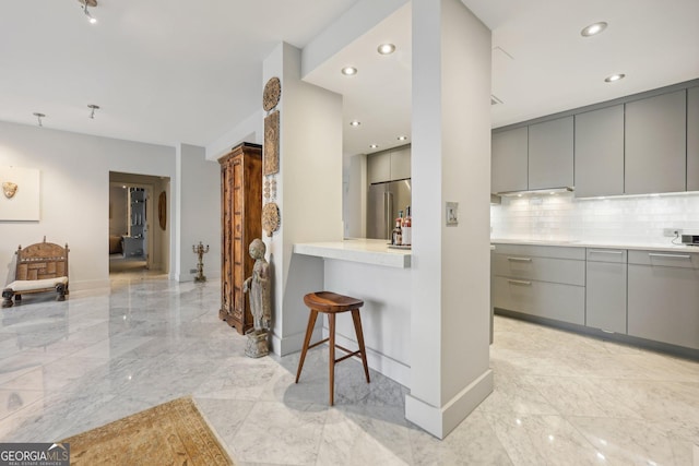 kitchen featuring gray cabinetry, a kitchen breakfast bar, high quality fridge, decorative backsplash, and kitchen peninsula