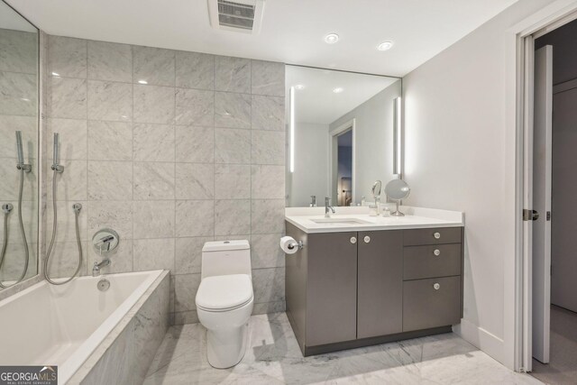 bathroom with tiled tub, vanity, tile walls, and toilet