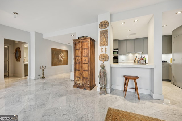 kitchen featuring gray cabinetry, backsplash, a breakfast bar area, and kitchen peninsula