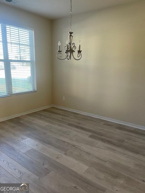 spare room featuring wood-type flooring and an inviting chandelier