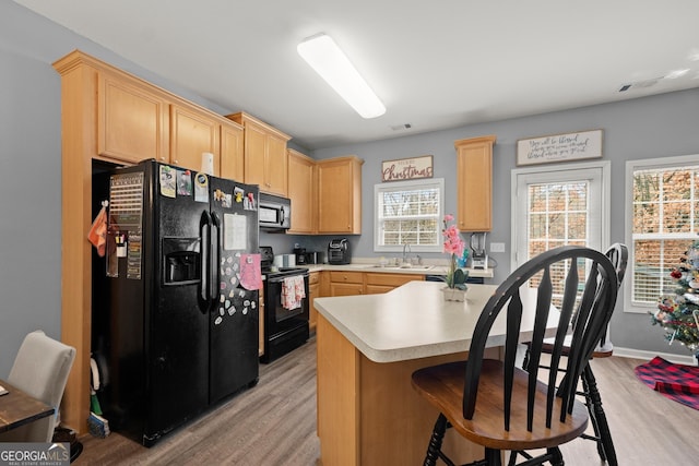 kitchen featuring a kitchen bar, light brown cabinetry, sink, black appliances, and light hardwood / wood-style flooring