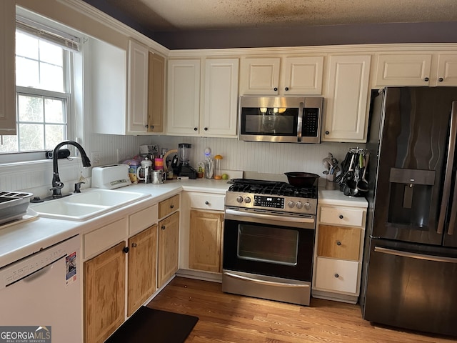 kitchen featuring appliances with stainless steel finishes, sink, a textured ceiling, and light hardwood / wood-style flooring