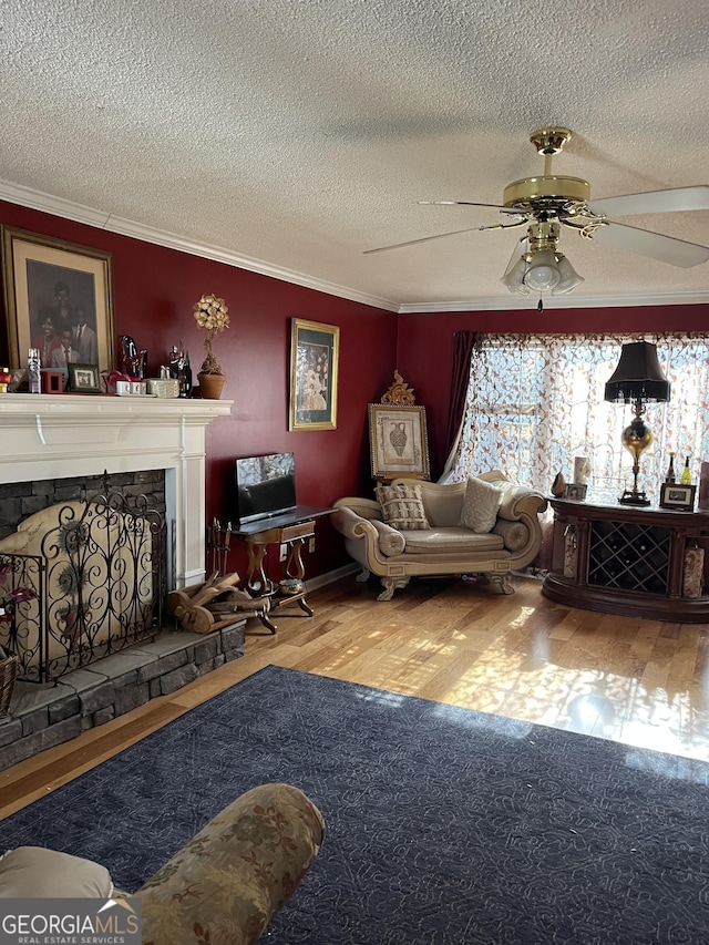 living room featuring a stone fireplace, crown molding, a textured ceiling, hardwood / wood-style flooring, and ceiling fan