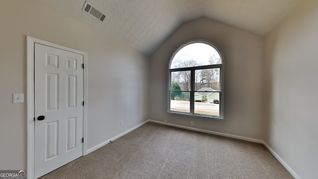 unfurnished room featuring carpet floors, a textured ceiling, and vaulted ceiling