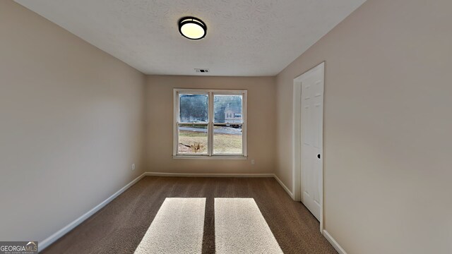 unfurnished room with dark colored carpet and a textured ceiling