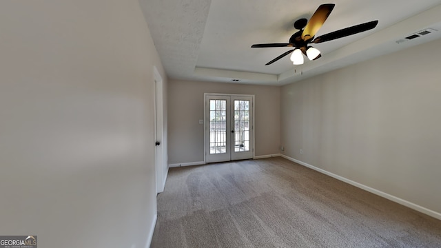 unfurnished room with light carpet, french doors, a tray ceiling, and ceiling fan