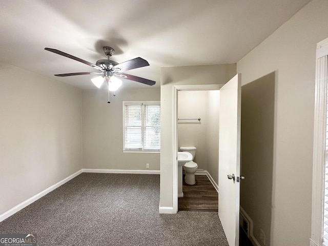 unfurnished bedroom with ensuite bath, ceiling fan, and dark carpet