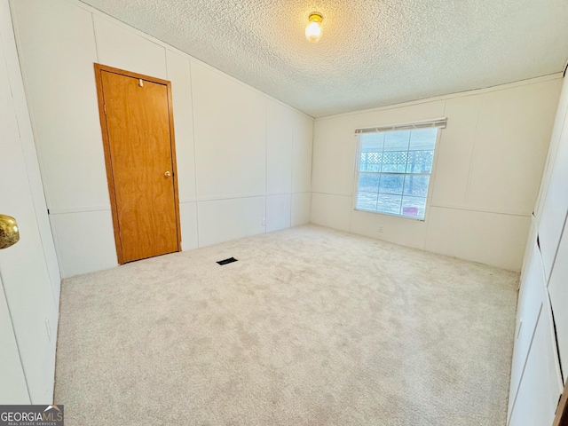 spare room featuring carpet floors, a decorative wall, and a textured ceiling