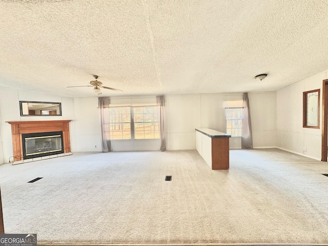 unfurnished living room featuring a glass covered fireplace, carpet flooring, ceiling fan, and a textured ceiling