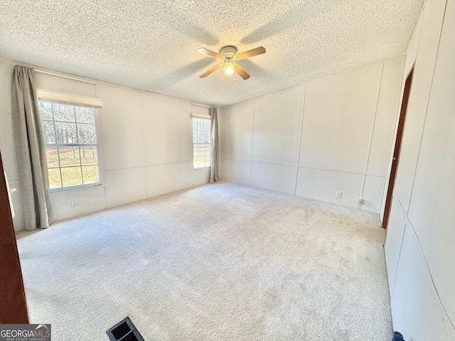 carpeted empty room featuring ceiling fan, a decorative wall, and a textured ceiling