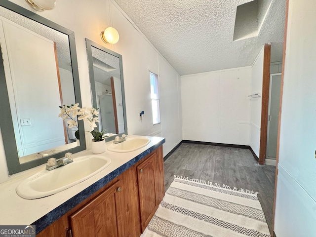 full bath with a sink, a textured ceiling, a shower stall, and wood finished floors