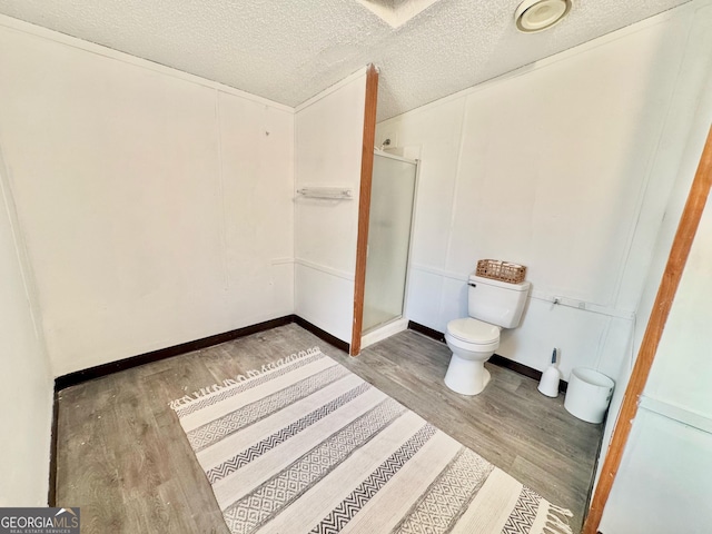 full bathroom featuring a textured ceiling, wood finished floors, toilet, and a shower stall