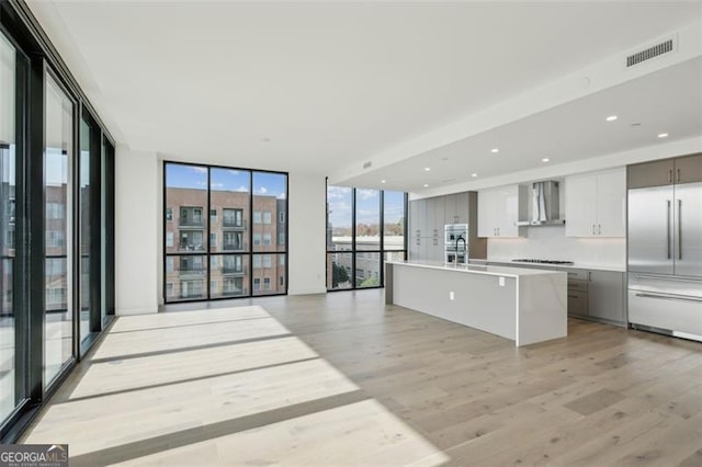 kitchen featuring expansive windows, a kitchen island, wall chimney range hood, light hardwood / wood-style flooring, and built in refrigerator