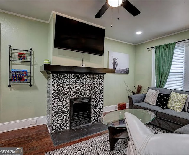 living room featuring a tile fireplace, wood-type flooring, ceiling fan, and ornamental molding