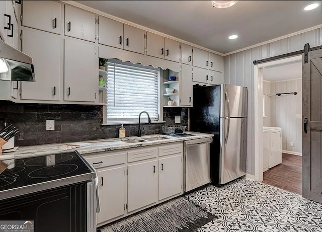 kitchen featuring washing machine and clothes dryer, sink, a barn door, ventilation hood, and appliances with stainless steel finishes