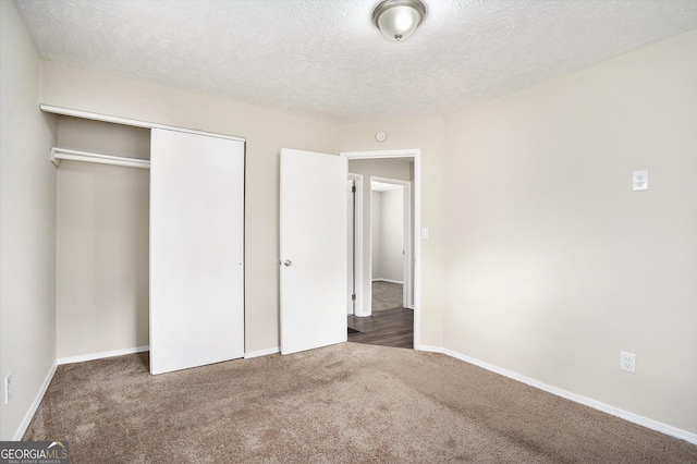 unfurnished bedroom featuring dark colored carpet, a textured ceiling, and a closet